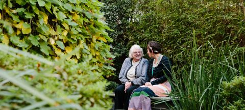 Caregiver and resident smiling and chatting in a green garden at Mercy Place Parkville