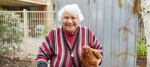 Female resident smiling with a chicken in her arms at Mercy Place Albury