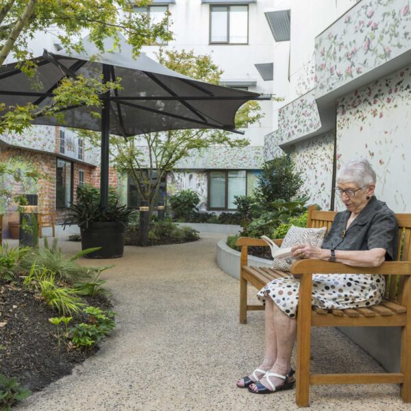 Female resident at Mercy Place East Melbourne, reading a book on a garden bench, in the picturesque internal courtyard.